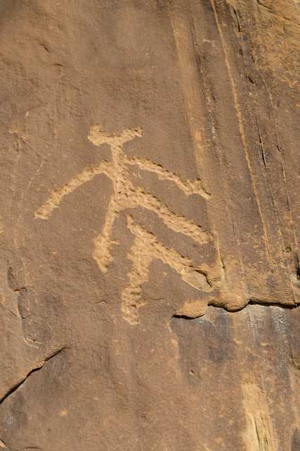 An abstract figure with outstretched arms is carved into a rock surface.