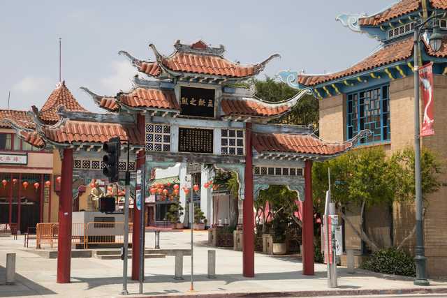 An ornate gate features Chinese characters on a black sign, topped with curved red-tiled roofs and supported by red pillars.