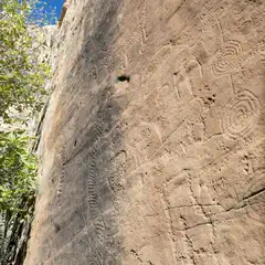 A rock face is covered with petroglyphs, including human figures and spiral designs.