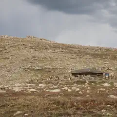 A small stone building stands in front of a rocky hillside under a cloudy sky.
