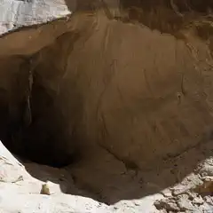 A large hole in a rock face is visible, surrounded by tan and brown stone.