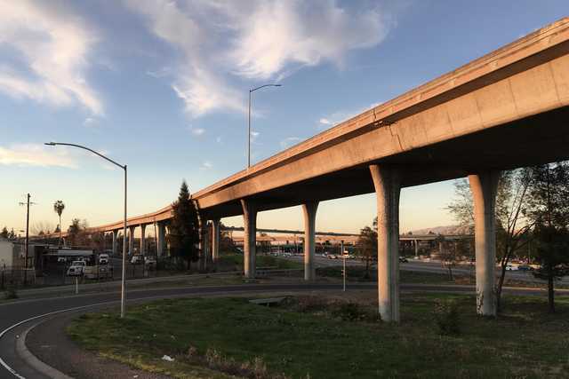 An elevated concrete highway spans over a grassy area, supported by numerous columns.