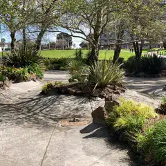 A concrete path runs through a garden with various plants and trees.