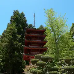 A traditional Japanese temple with multiple tiers and a red roof nestled among lush greenery including tall trees and manicured shrubs.