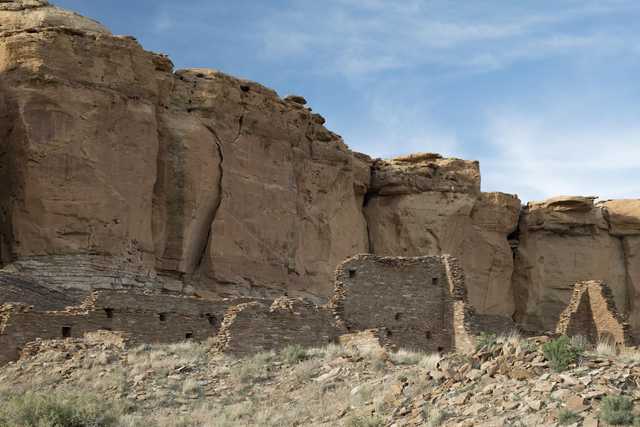 A stone ruin stands at the base of tall, eroded rock formations.