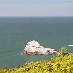 A rocky outcrop jutting into the ocean, surrounded by green foliage and calm waters.