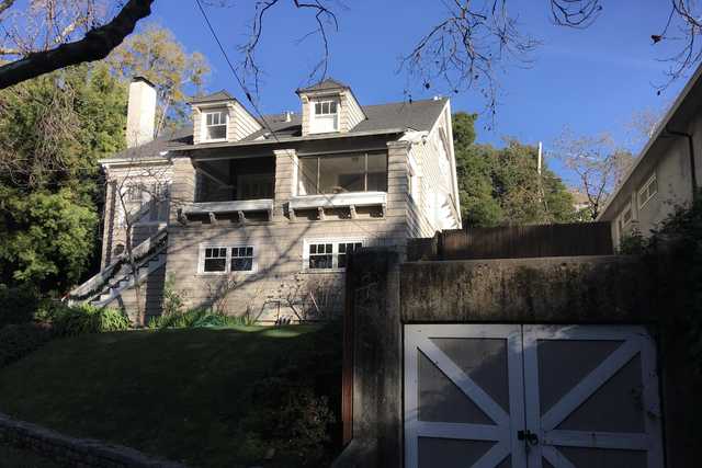 An off-white house with gray shingles and white trim with a chimney, a covered porch, and a staircase leading to a second floor balcony.