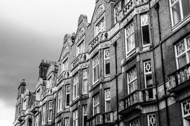 A row of ornate brick townhouses with decorative gables, bay windows, and stone carvings, captured from a low angle.
