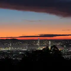 A panoramic view of a coastal city at dusk, featuring a prominent bridge spanning a bay, illuminated urban areas, and a distant mountainous horizon.