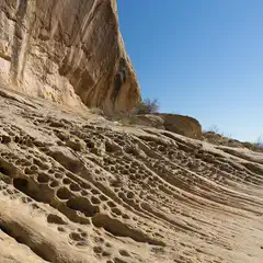 An eroded rock face featuring a prominent outcropping with a sloping surface marked by numerous holes and grooves.