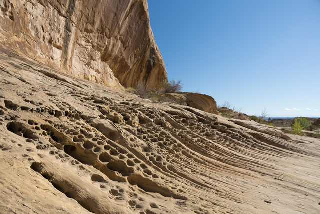 An eroded rock face featuring a prominent outcropping with a sloping surface marked by numerous holes and grooves.