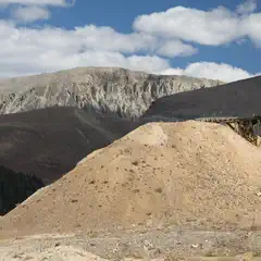 An old wooden structure is visible on top of a pile of dirt and debris at the edge of a mountainous landscape.