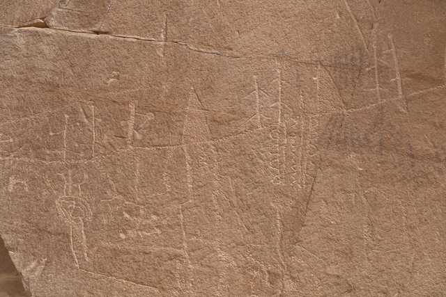 A rock surface features ancient petroglyphs, including geometric shapes and abstract designs.