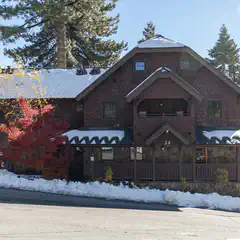 A two-story building with brown shingle siding and a covered porch, featuring a dark roof and several windows.