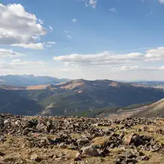 A rocky hillside under a partly cloudy sky, with distant mountains and valleys visible.