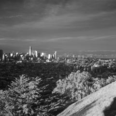 A densely populated city skyline with numerous skyscrapers. A large suspension bridge spans a body of water in the background.