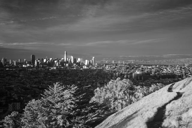 A densely populated city skyline with numerous skyscrapers. A large suspension bridge spans a body of water in the background.