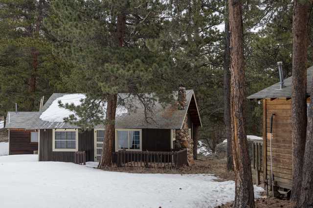 A group of rustic cabins nestled among tall trees with snow on the ground and roofs.