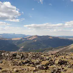 A rocky hillside under a partly cloudy sky, with distant mountains and valleys visible.