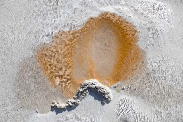 A circular area of orange and brown sediment is surrounded by white, textured ground.