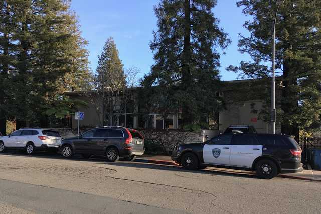 A police SUV parked on a street in front of a building with trees in the background.
