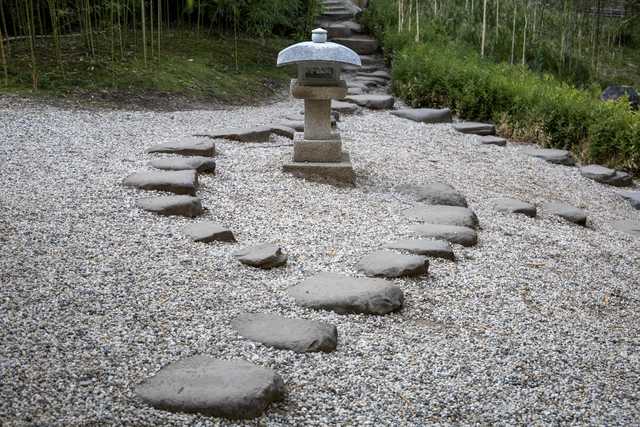 A stone lantern stands on a bed of small white pebbles, surrounded by stepping stones arranged in a curved path.