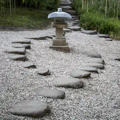 A stone lantern stands on a bed of small white pebbles, surrounded by stepping stones arranged in a curved path.
