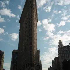 A tall, triangular building with many windows and a pointed roof. The sky is partly cloudy above it.