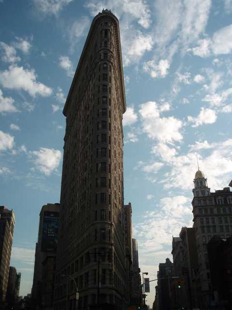 A tall, triangular building with many windows and a pointed roof. The sky is partly cloudy above it.