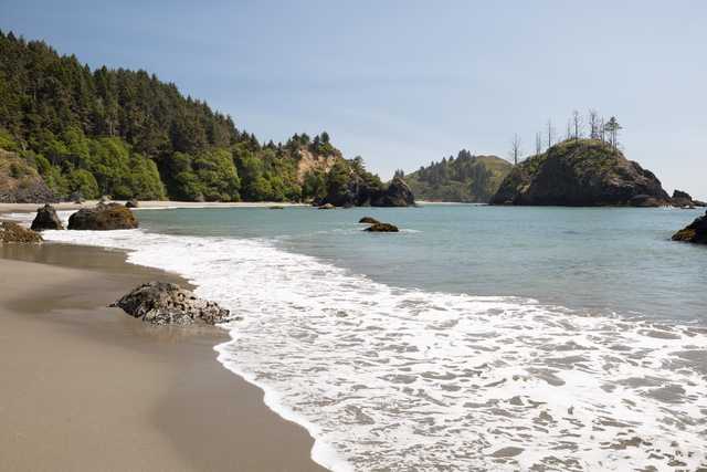 A sandy beach curves toward a cove with green hills on either side.