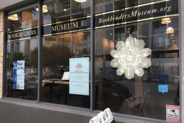 An entrance to a building is visible through a window with a large white flower-shaped light fixture hanging from it.