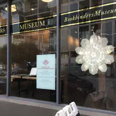 An entrance to a building is visible through a window with a large white flower-shaped light fixture hanging from it.