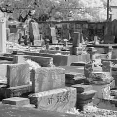 A cemetery contains numerous headstones and grave markers, some of which are weathered and worn.