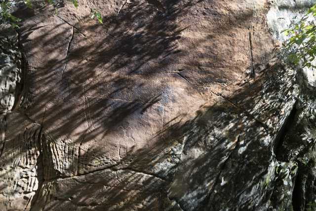 A large rock face, featuring several cracks and crevices and a humanoid petroglyph.