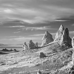 A stark, barren landscape features jagged rock formations rising from a salt flat under a partly cloudy sky.