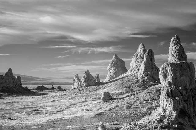 A stark, barren landscape features jagged rock formations rising from a salt flat under a partly cloudy sky.