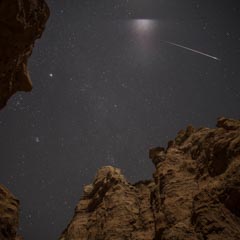 A rocky cliff face at night with a starry sky and a shooting star.