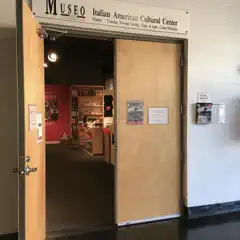 A wooden door is open to reveal a room filled with shelves of books and various objects.