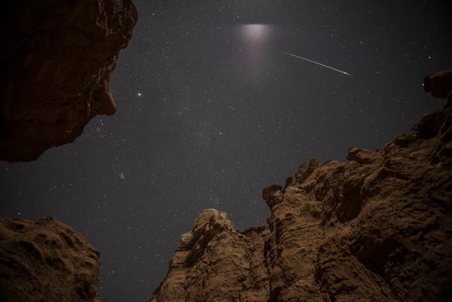 A rocky cliff face at night with a starry sky and a shooting star.