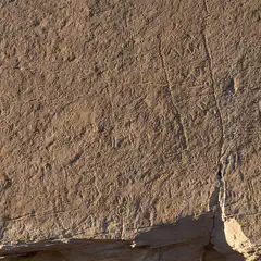 A large rock face, featuring numerous scratches and marks etched into its surface.