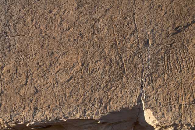 A large rock face, featuring numerous scratches and marks etched into its surface.
