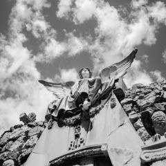A statue of an angel with outstretched wings, on a rocky surface under a partly cloudy sky.
