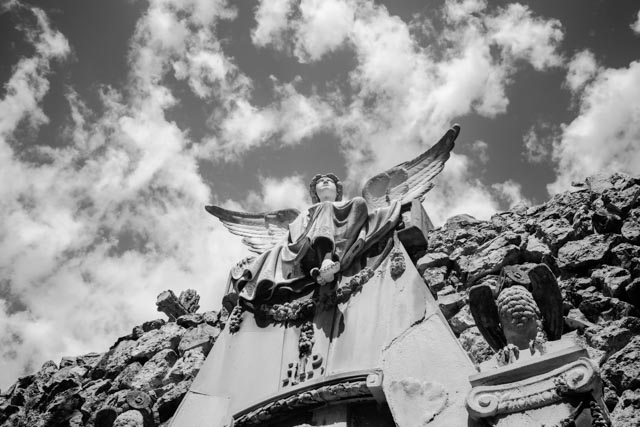 A statue of an angel with outstretched wings, on a rocky surface under a partly cloudy sky.