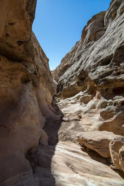 A narrow, winding canyon is carved into tan-colored rock.