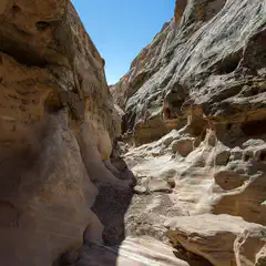A narrow, winding canyon is carved into tan-colored rock.