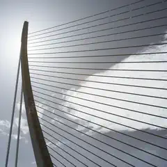 A bridge with a curved arch and metal cables against a cloudy sky.