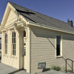 A small, light-colored wooden building with decorative trim around the door and windows.