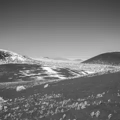A volcanic landscape with snow-covered hills and sparse vegetation is visible under a clear sky.