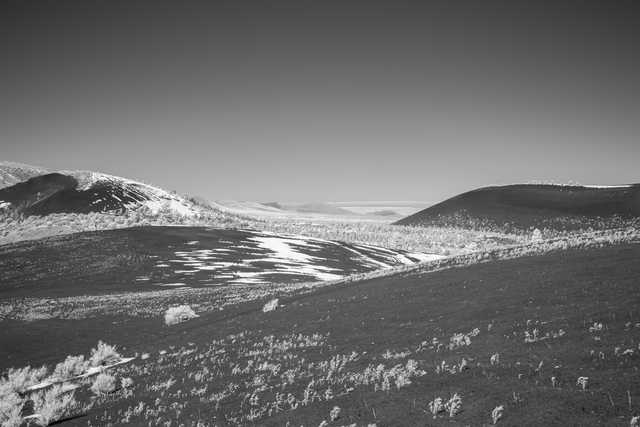 A volcanic landscape with snow-covered hills and sparse vegetation is visible under a clear sky.