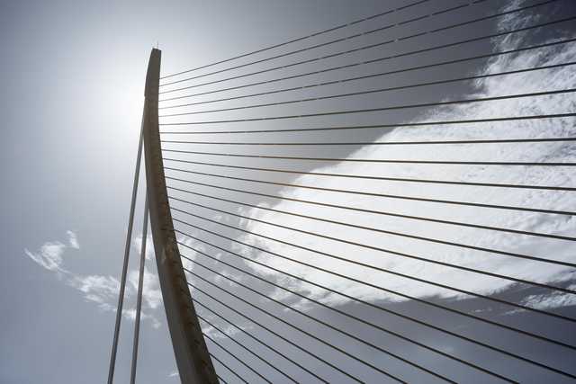 A bridge with a curved arch and metal cables against a cloudy sky.